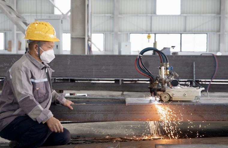 Operator preparing the edge of a steel plate with a grinder before finishing